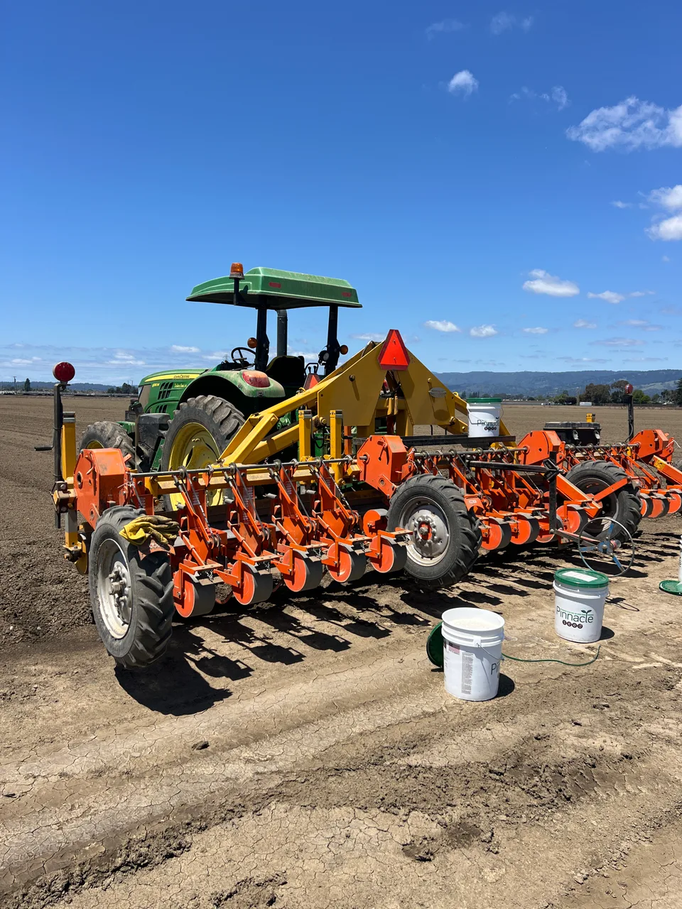 A tractor and orange multi-row planting equipment in a prepared field.