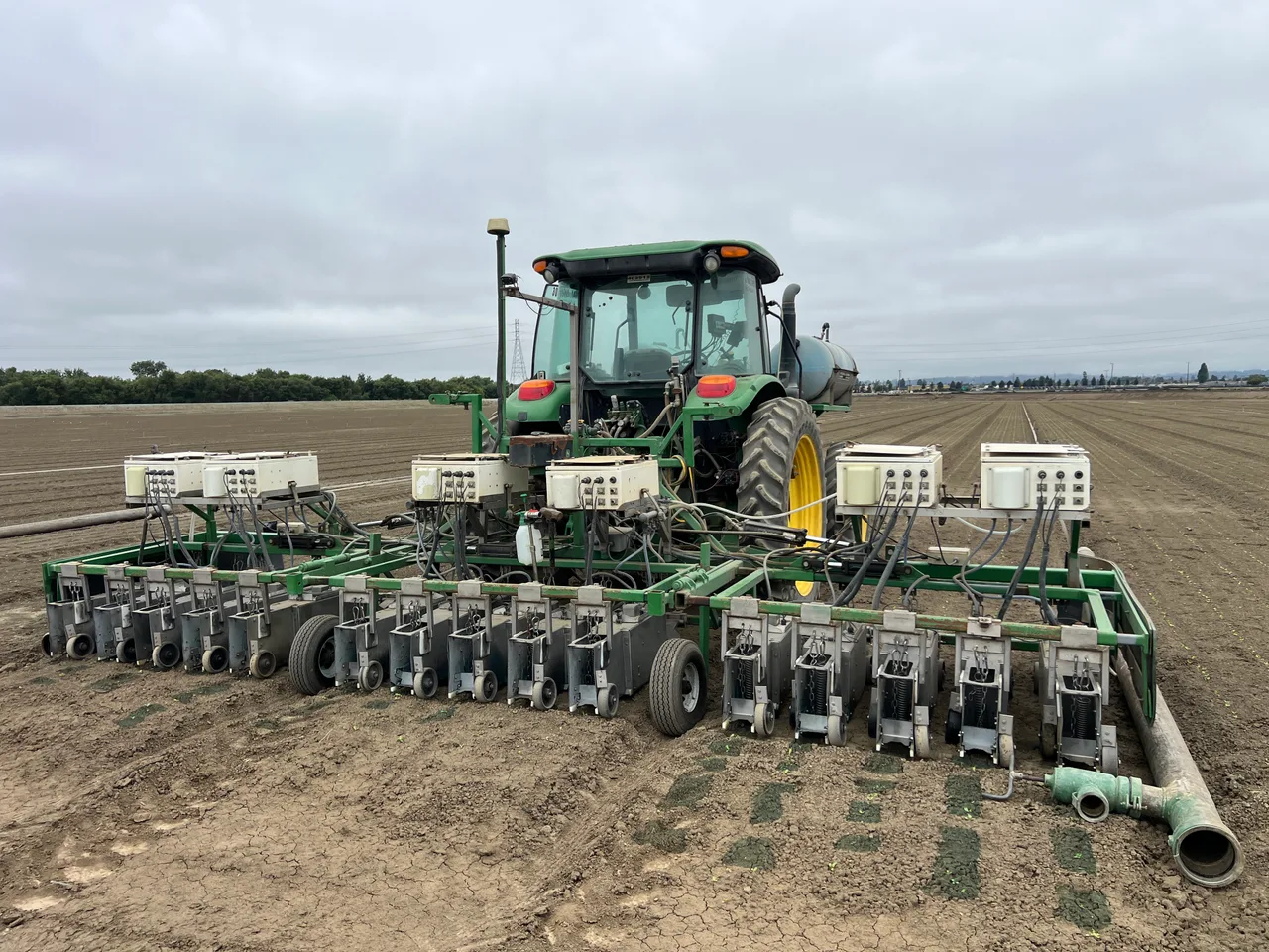 A tractor with a multi-row implement and electronic control units in a vegetable field.